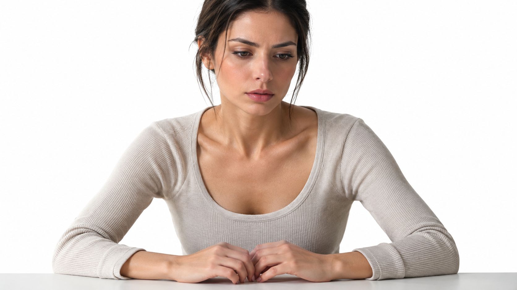 A concerned woman sitting at a table looking down, conveying a mood of worry and stress.